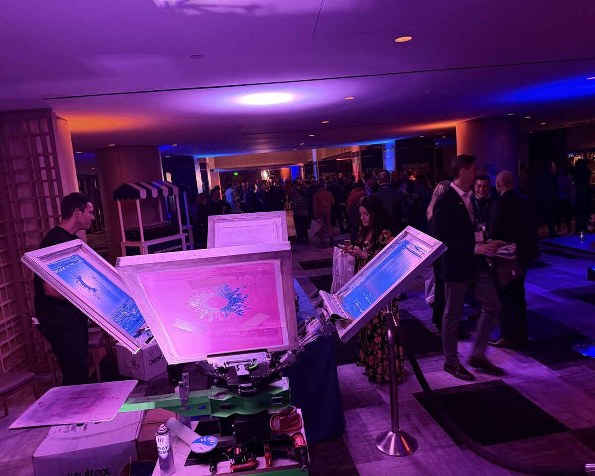 Wide view of glowing print screens with a full party crowd behind them